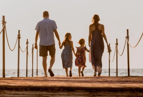 Consulenza genitorialità. Nell'immagine una famiglia si tiene per mano camminando verso il mare.
